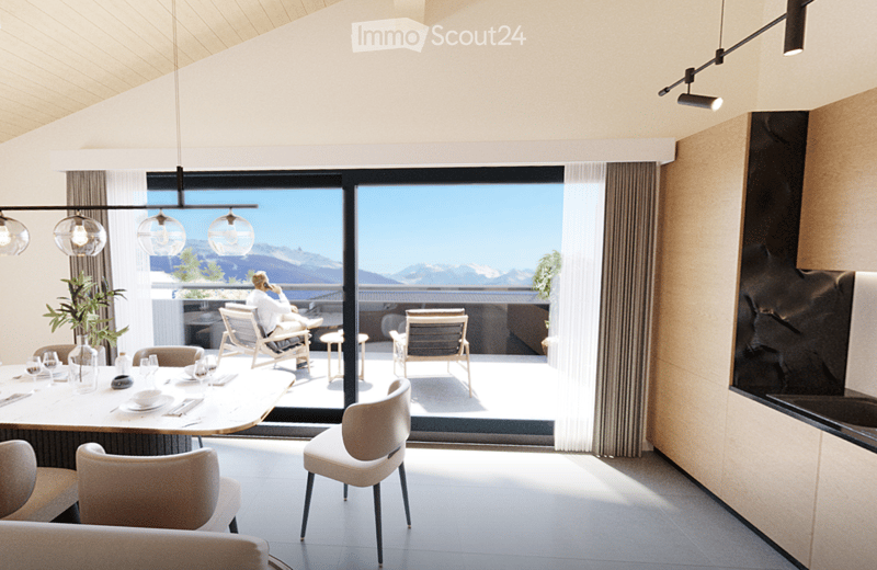 Modern dining area with a round table, chairs, and a view of mountains through large windows. There is a sofa and a plant in the foreground, and a person is sitting on a chair outside on the balcony.
