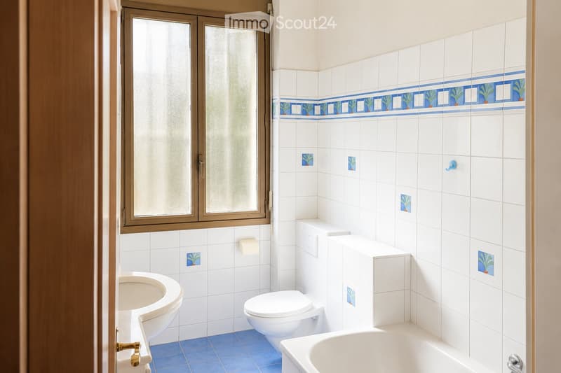 Bathroom with white tiles, blue accents, bathtub, toilet, sink, and a window with frosted glass.