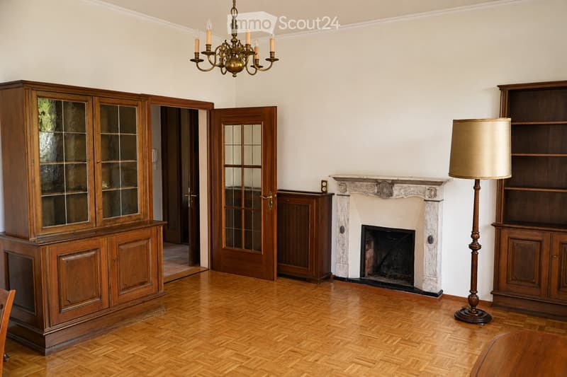 Elegant living room with wooden flooring, a marble fireplace, wooden cabinetry, a chandelier, and a floor lamp.