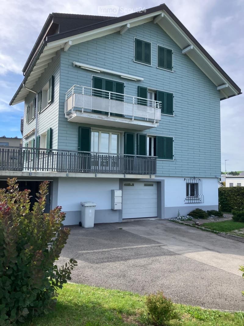 Two-story house with light blue exterior, green shutters, balconies, garage, and driveway.