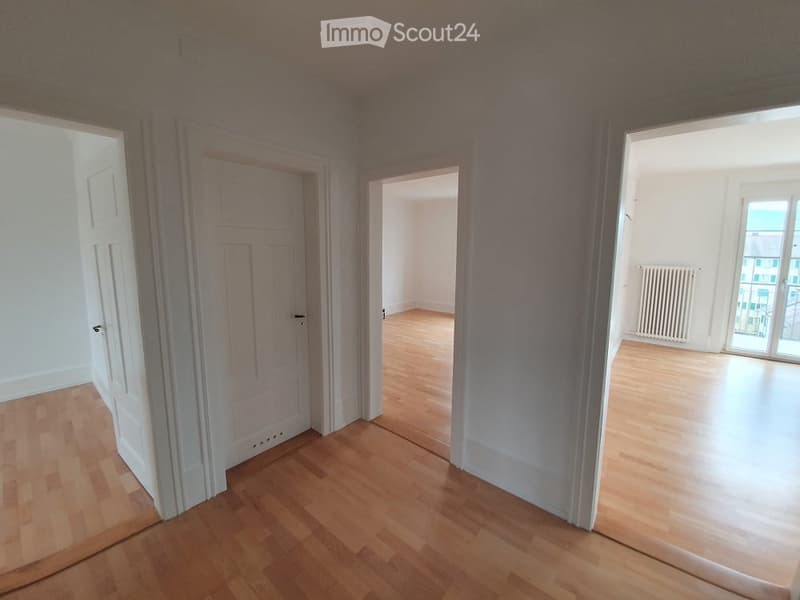 Empty room with wooden flooring, white walls, and multiple doors leading to other spaces.