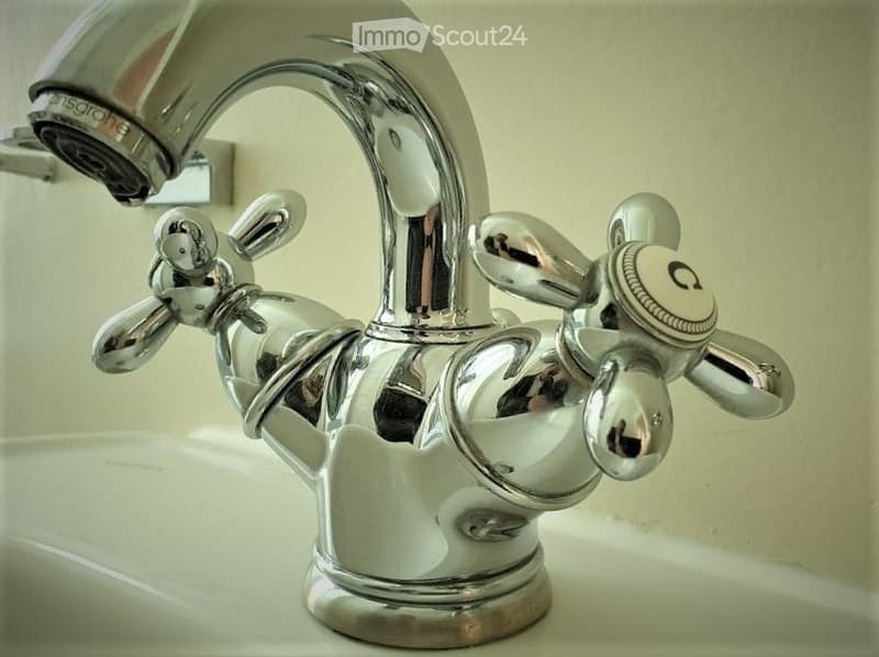 Close-up of a chrome faucet with dual handles and a spray function, mounted on a white sink.