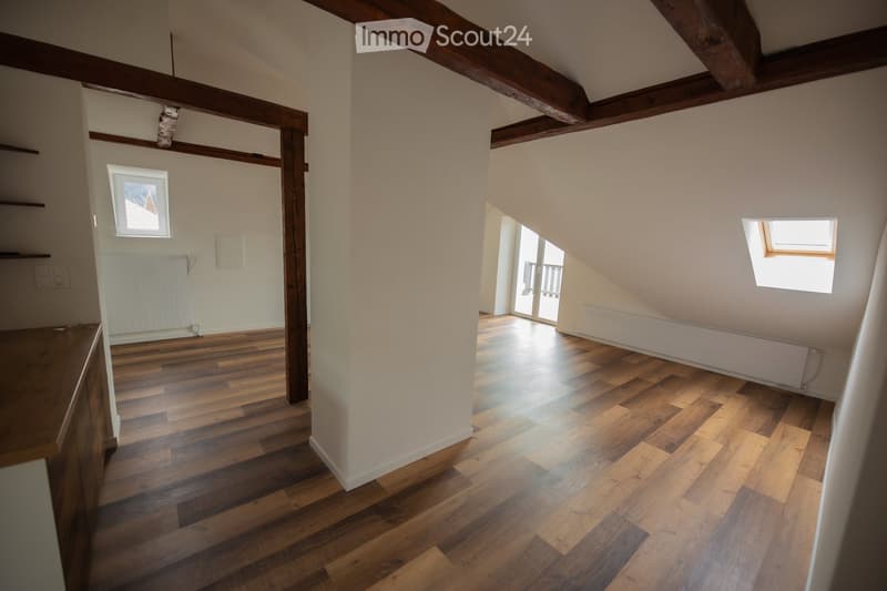 Empty attic space with wooden beams, wooden flooring, and natural light from skylights and windows. No furniture or furnishings present.
