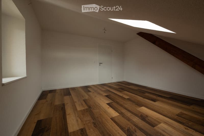 Empty attic room with wooden flooring, white walls, and a skylight window. No furniture or equipment present.