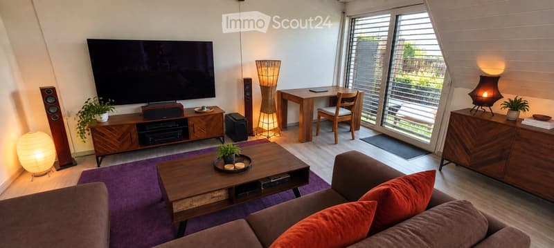 Modern living room with a large TV, wooden coffee table, sofa with red cushions, floor lamps, and a desk area with a chair.