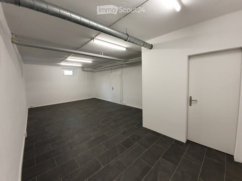Empty room with white walls, dark tiled floor, and exposed pipes on the ceiling. No furniture or equipment.