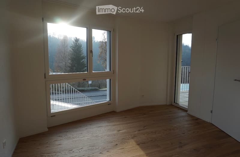 Empty room with wooden flooring, large windows, and a sliding glass door leading to a balcony.