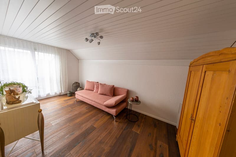 A cozy living room with wooden flooring, a pink sofa, a small round table, a plant, and decorative items.