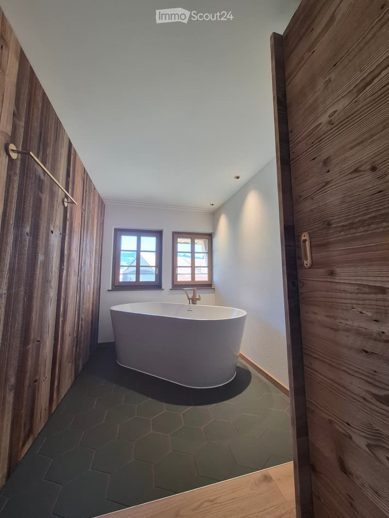 Modern bathroom with a freestanding bathtub, wooden walls, and two windows offering a view.