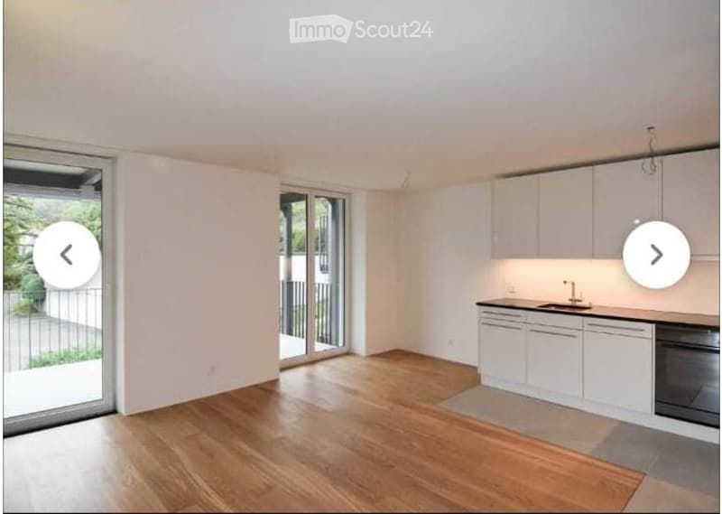 Bright, unfurnished kitchen with white cabinets, wooden flooring, and large sliding glass doors leading to a balcony.