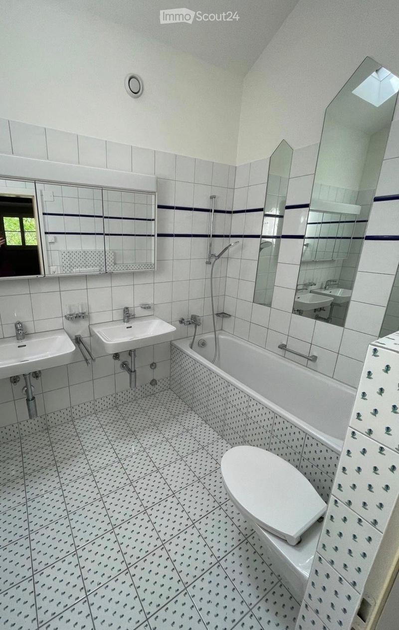 Bathroom with white tiles, two sinks, a bathtub, a toilet, and mirrors above the sinks.