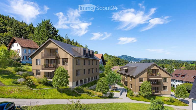 A multi-story residential building with balconies, surrounded by greenery and trees, with a clear blue sky in the background.