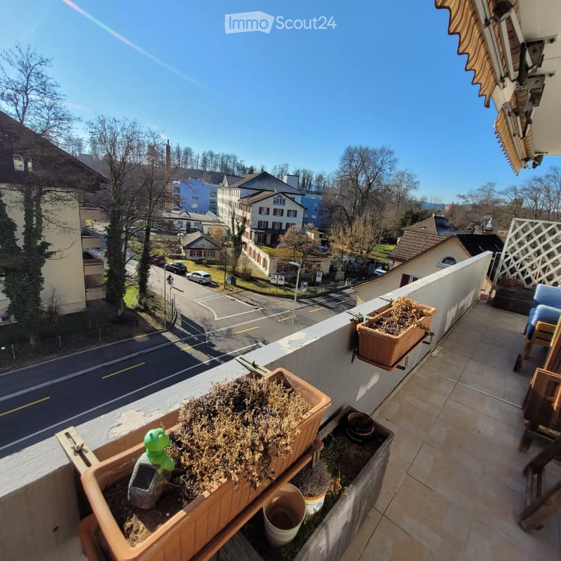 Balcony with tiled floor, potted plants, and a view of the street and surrounding buildings.