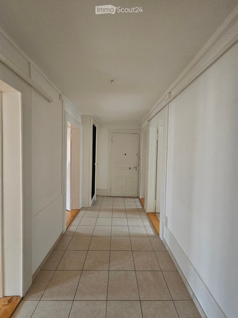 Empty hallway with tiled floor, white walls, and several doors leading to other rooms.