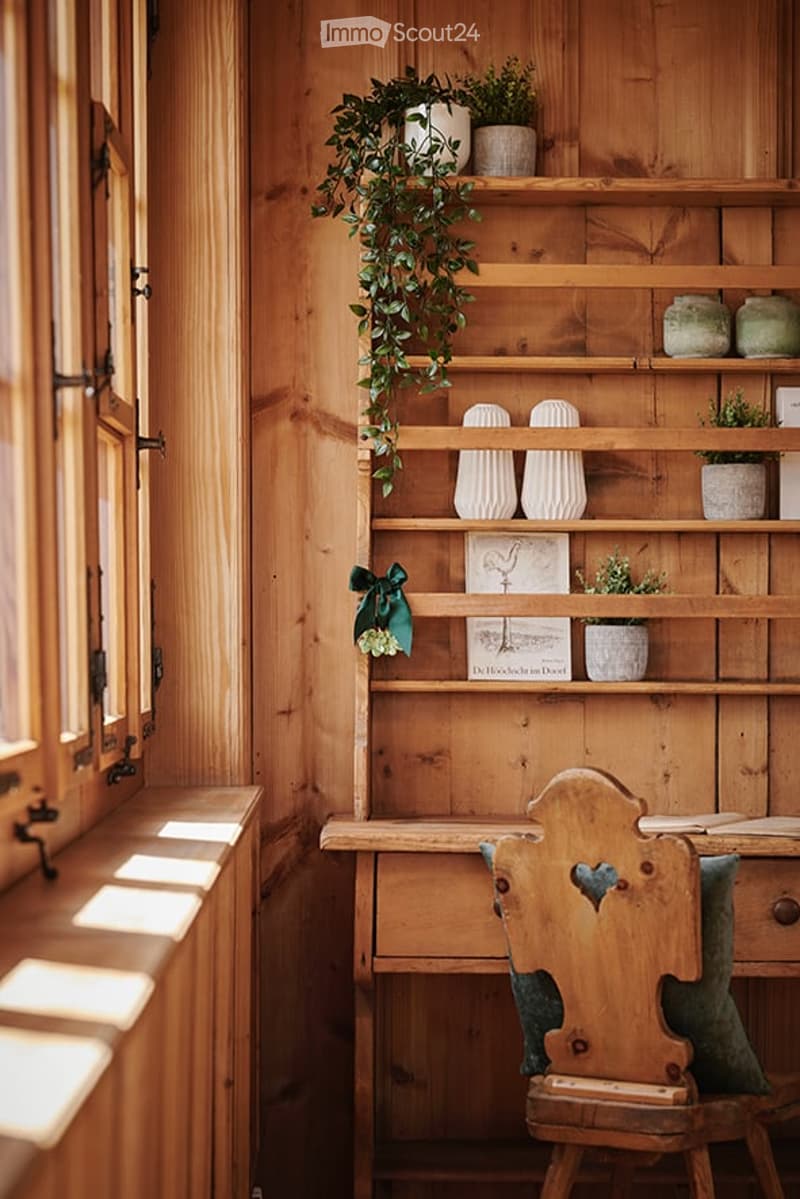 Cozy wooden room with a wooden chair, a wooden shelf with vases and potted plants, and a book on the shelf.