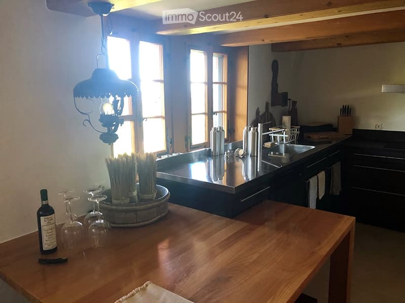 Bright kitchen with wooden table, wine bottle, wine glasses, stainless steel sink, and dark cabinets.
