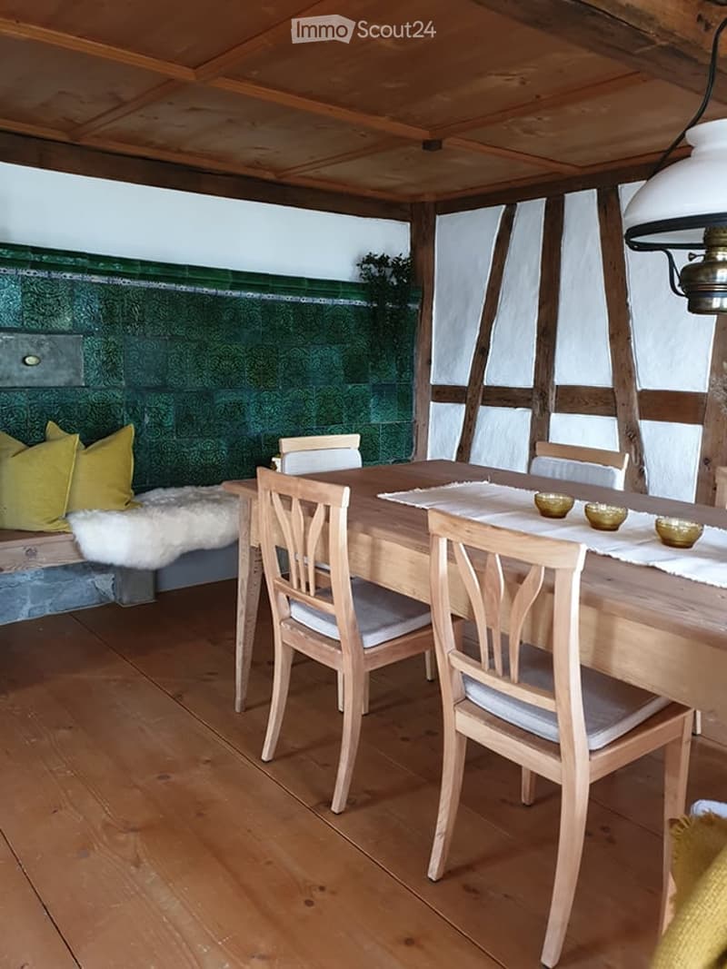 A cozy, wooden-floored dining area with a dining table, chairs, a sofa with pillows, and decorative bowls on the table.