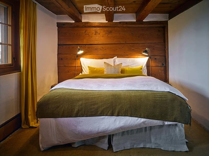 Cozy bedroom with a wooden headboard, a large bed with white and yellow bedding, and wall-mounted lamps on either side of the bed.