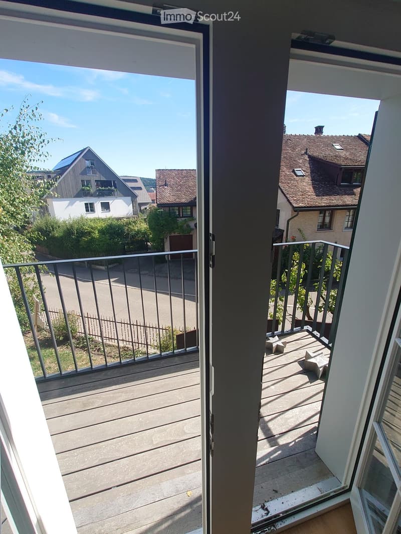 Balcony with wooden decking, metal railing, and a view of the neighborhood with houses and greenery.