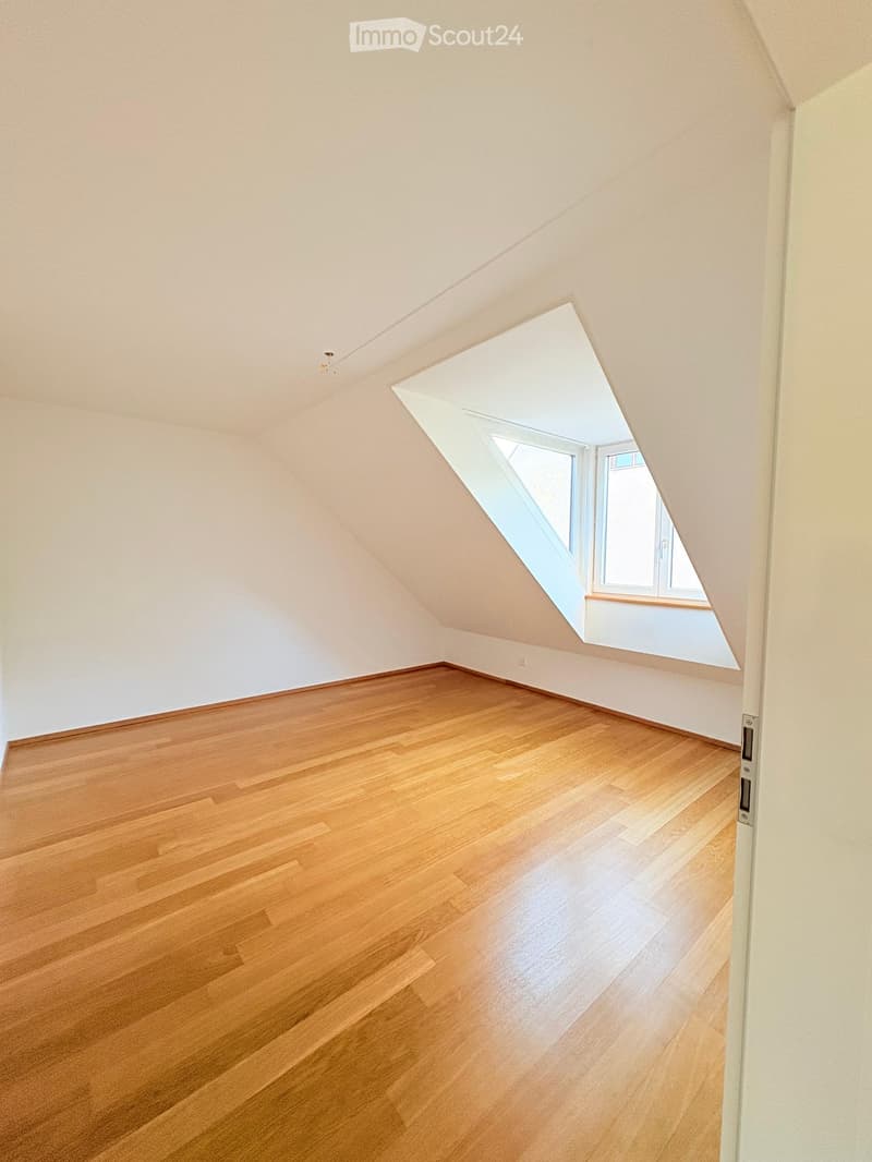 Empty attic room with wooden flooring and a skylight window, featuring white walls and a sloped ceiling.