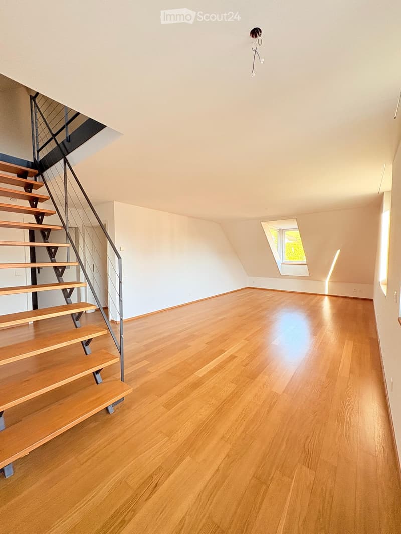 Empty room with wooden flooring, white walls, and a staircase leading upwards. A skylight window provides natural light.