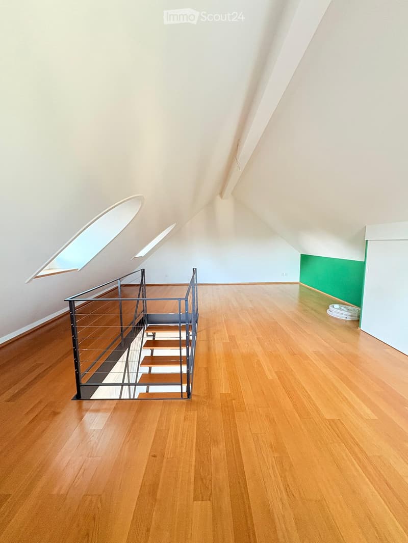 Empty attic space with wooden flooring, a metal staircase leading upwards, and a skylight window providing natural light.