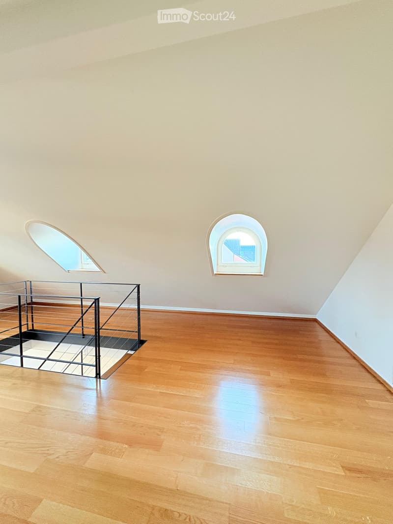 Empty room with wooden flooring, light-colored walls, and two arched windows near the ceiling.