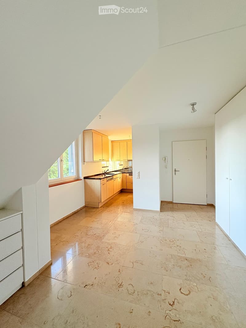 Bright, open room with a kitchen area featuring light wooden cabinets, a sink, and a dishwasher. The floor is tiled with a decorative pattern, and there is a window with a wooden sill on the left side.