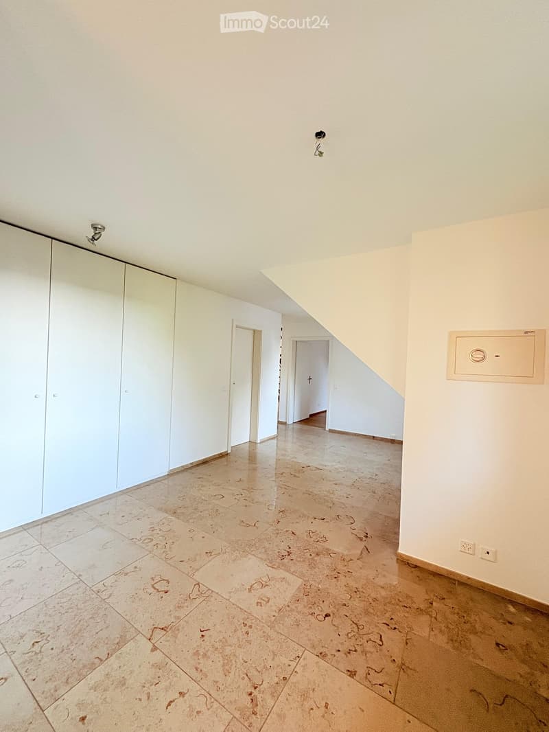 Empty hallway with light-colored tiled flooring, white walls, and two doors leading to other rooms. The hallway features a large mirrored closet on one side and a staircase leading upwards.