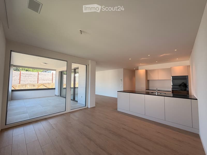 Modern kitchen with white cabinets, a black countertop, and a sink, connected to a tiled patio through large glass doors.