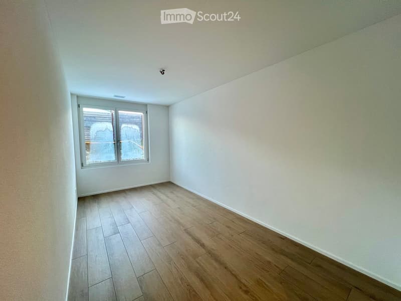 Empty room with light-colored walls and wooden flooring, featuring a single window with frosted glass panels.