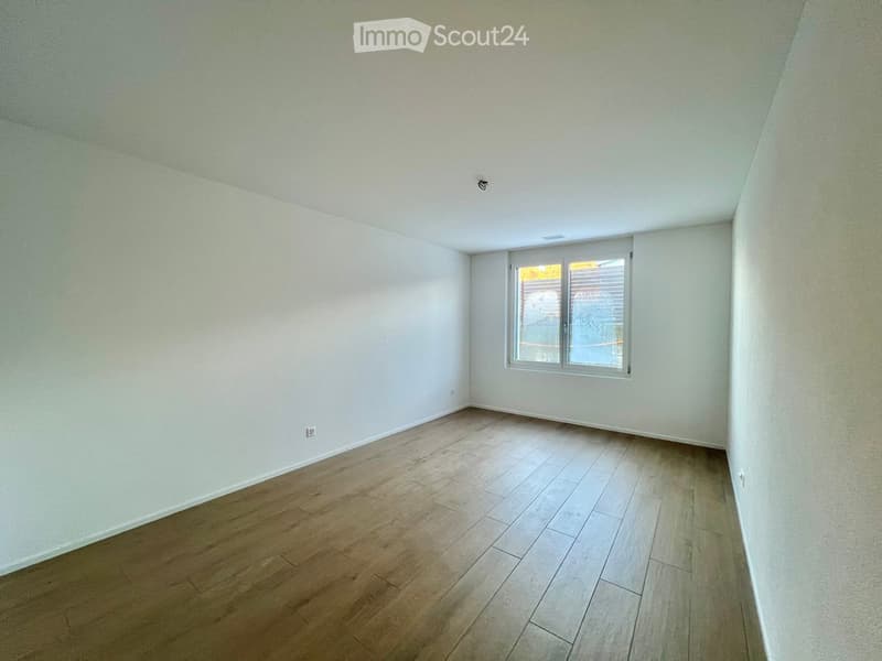 Empty room with light-colored walls and wooden flooring, featuring a single window with blinds.