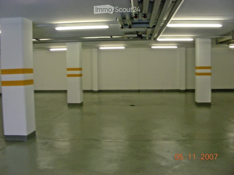 Empty underground parking area with white pillars, fluorescent lighting, and a smooth concrete floor.
