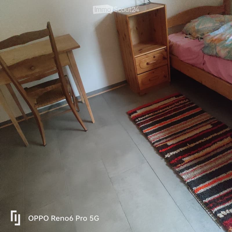 Bedroom with a wooden bed, nightstand, chair, and a colorful striped rug on the floor.
