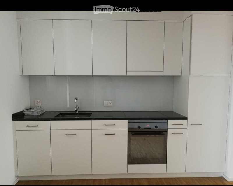 Modern kitchen with white cabinets, black countertops, a sink, and an oven. The space is clean and contemporary with a wooden floor.