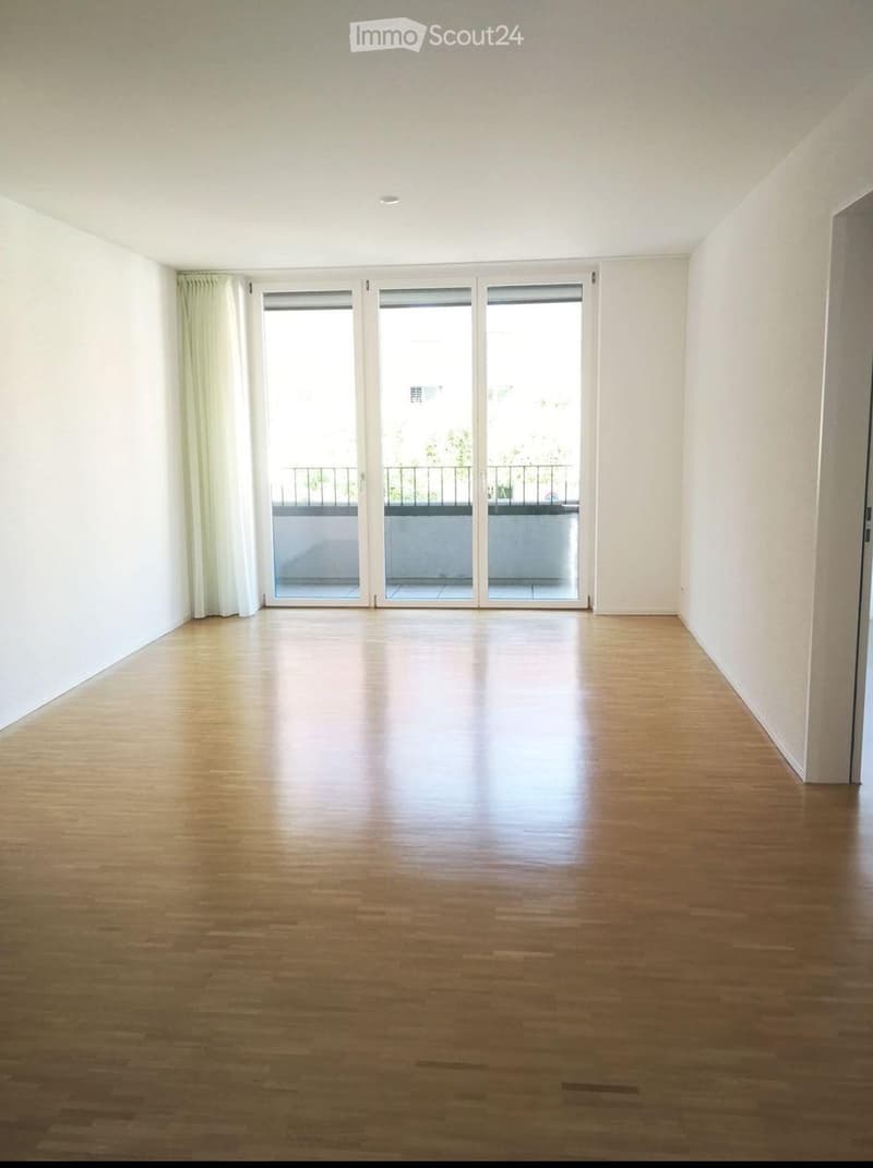 Empty room with wooden flooring, white walls, large sliding glass doors leading to a balcony.