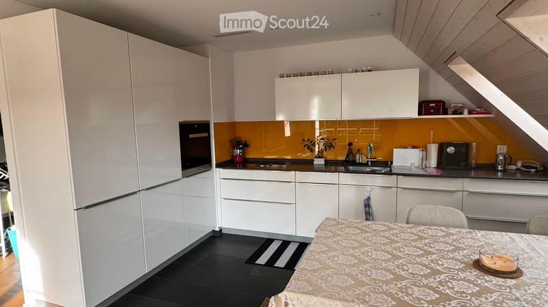 Modern kitchen with white cabinets, black countertops, and a yellow backsplash. Features a refrigerator, oven, sink, and a small dining area with a table and chairs.