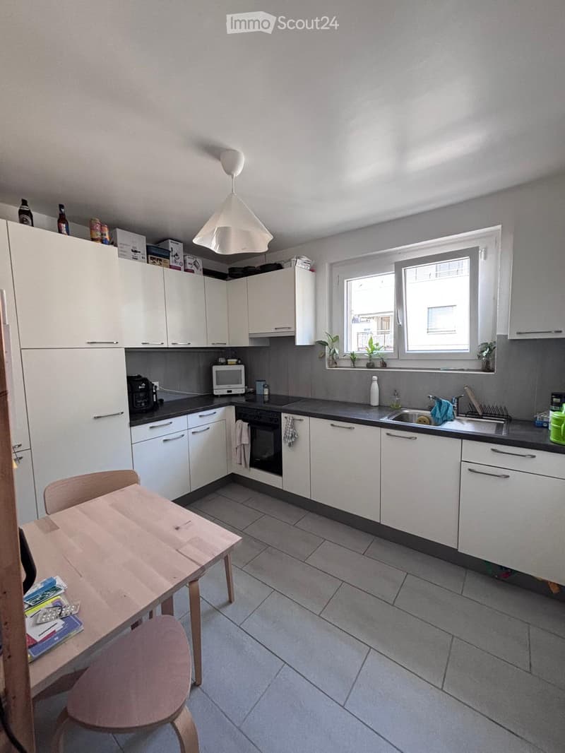 Modern kitchen with white cabinets, grey countertops, and a central island. Includes a refrigerator, microwave, oven, sink, and a small dining area with a table and chairs.