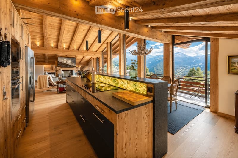 Modern kitchen with wooden beams, stainless steel appliances, large windows offering mountain views, and a central island with a countertop and seating area.