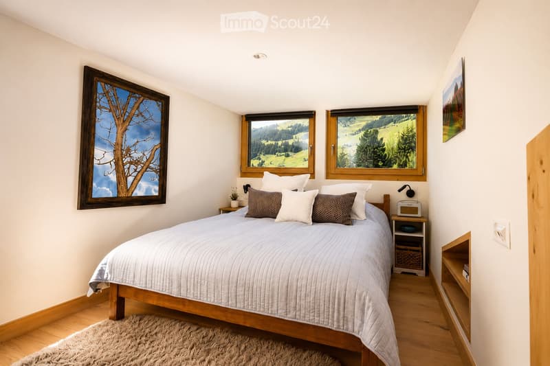 Cozy bedroom with a large bed, nightstand, and scenic windows overlooking a green landscape.