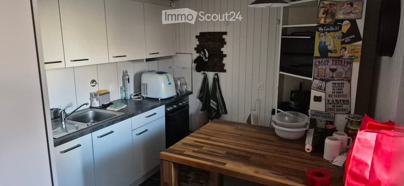 Modern kitchen with white cabinets, stainless steel sink, oven, toaster, and wooden island table with cups and bowls.