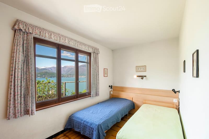 Cozy bedroom with two single beds, large window offering scenic mountain and lake view, wooden flooring, and decorative wall art.
