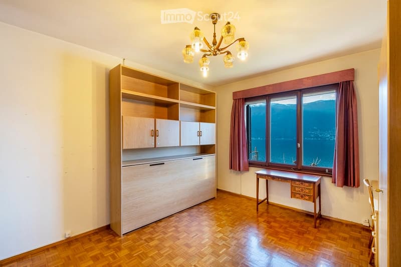 Bright room with wooden flooring, large window with a scenic view, wooden cabinet, small table, and chandelier.