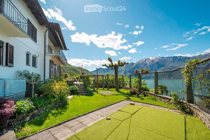 Well-maintained garden with green lawn, gravel pathways, small trees, shrubs, and a scenic mountain view in the background.