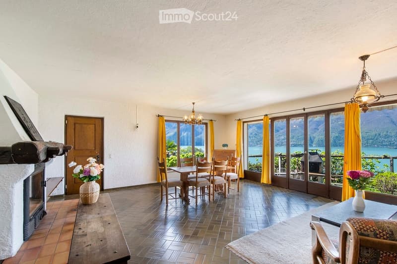 Bright dining area with wooden flooring, large windows offering scenic views, a dining table with chairs, a fireplace, and decorative vases.
