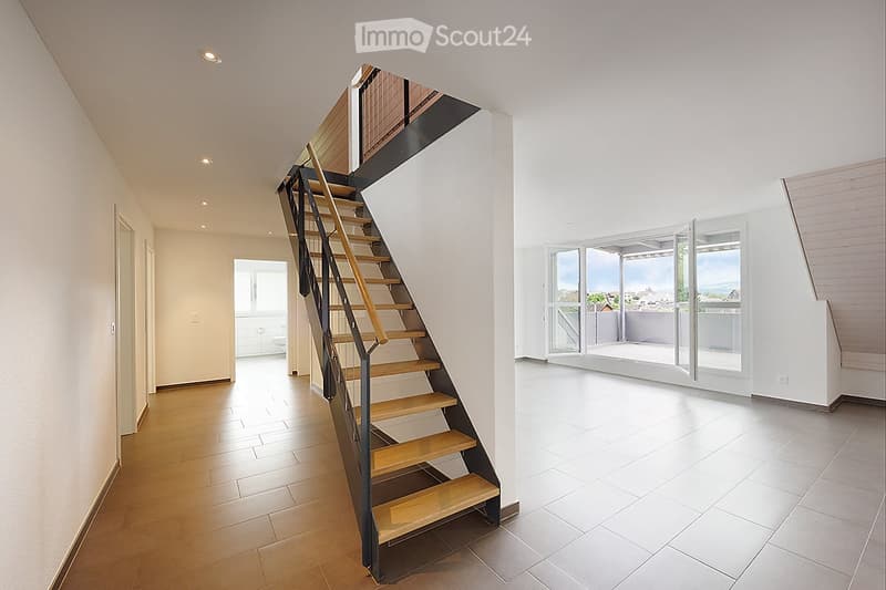 Modern hallway with wooden stairs, white walls, and large windows leading to a balcony with a scenic view.