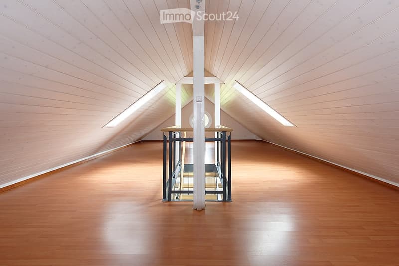 An empty attic space with wooden flooring and slanted wooden ceilings, featuring a small staircase leading upwards.