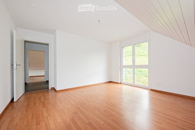 Empty room with wooden flooring, white walls, large windows, and an open door leading to another room.