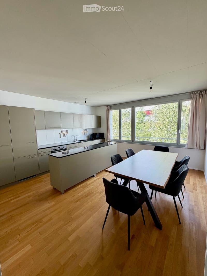 Modern kitchen and dining area with light wood flooring, grey cabinets, a central island, and a dining table with chairs.
