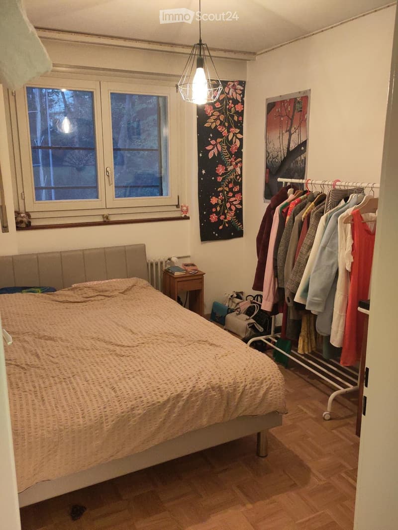 Cozy bedroom with a bed, nightstand, radiator, clothing rack, and artwork on the walls.